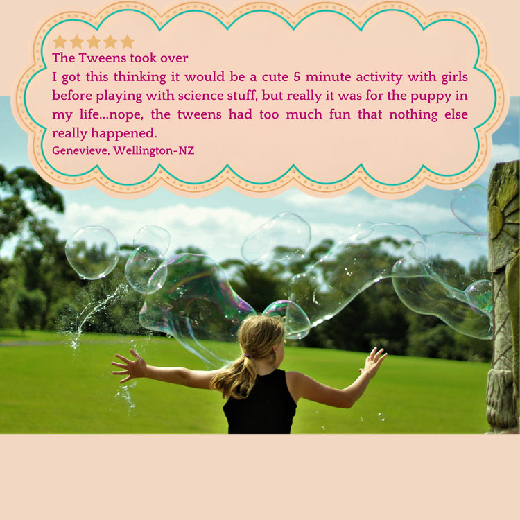 A little girl is playing outside on the green grass with giant bubbles