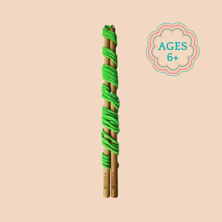 A wooden giant bubble wand wrapped in bright green yarn shown vertically on a warm beige background with a decorative 'AGES 6+' badge in the upper right.